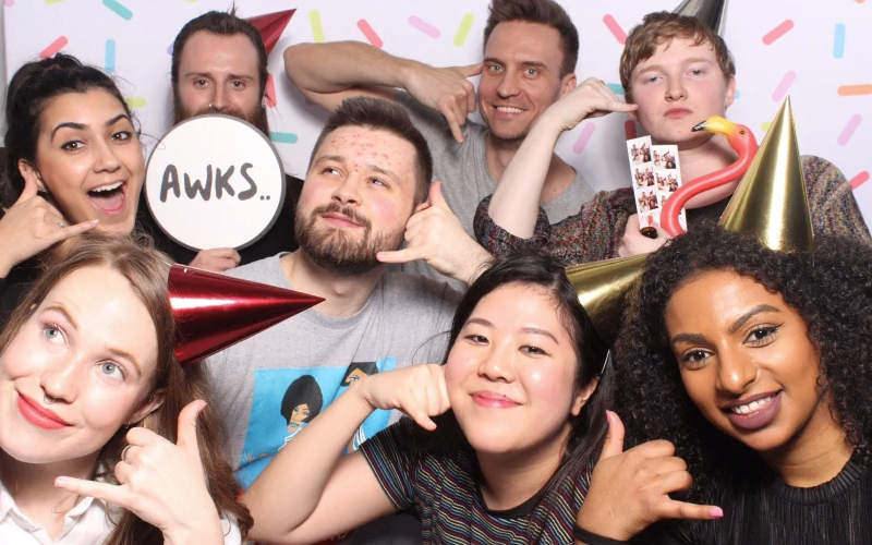 A group of people all making the 'call me' sign with their hands, some of them wearing party hats. Team Call and the Gang hav