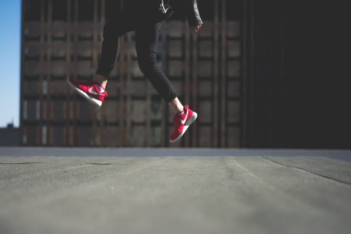 person wearing pair of red Nike shoes, jumping.