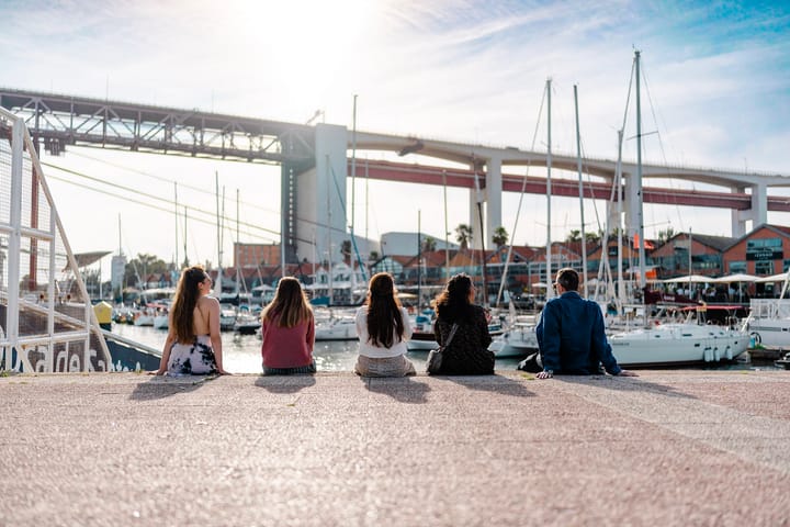 A photo of a group of five people, staring out at the marina, their backs to us in the audience. The sun is shining bright, t